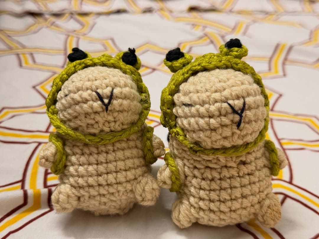 Two hand-crocheted plushies wearing little green frog hoodies
